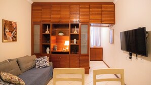 A living room with a sofa, chairs, wooden cabinets, a television, and a painting on the wall. - SUH Copacabana 71 Princess Beach (Rio de Janeiro)