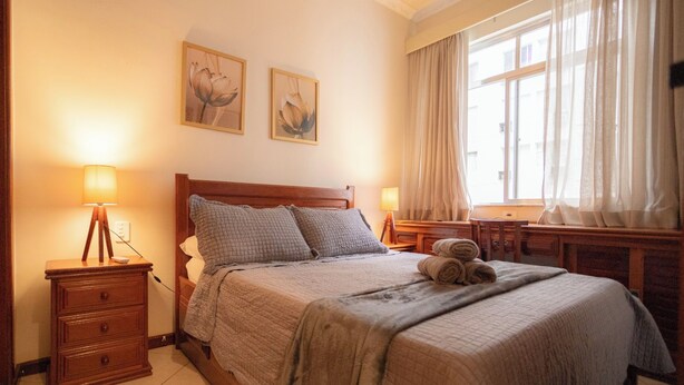 A neatly arranged bedroom with a bed, two bedside tables, a lamp, and a window with curtains. - SUH Copacabana 71 Princess Beach (Rio de Janeiro)