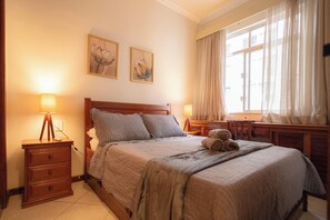 A neatly arranged bedroom with a bed, two bedside tables, a lamp, and a window with curtains. - SUH Copacabana 71 Princess Beach (Rio de Janeiro)