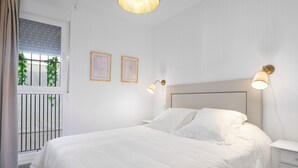 Une chambre avec un grand lit, deux lampes de chevet, une table de nuit, une fenêtre avec des stores et deux tableaux encadrés accrochés au mur.
