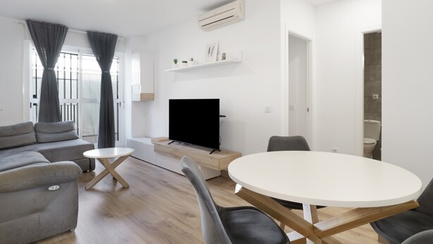 Un salon moderne avec un canapé gris, une table ronde blanche et un téléviseur à écran plat.