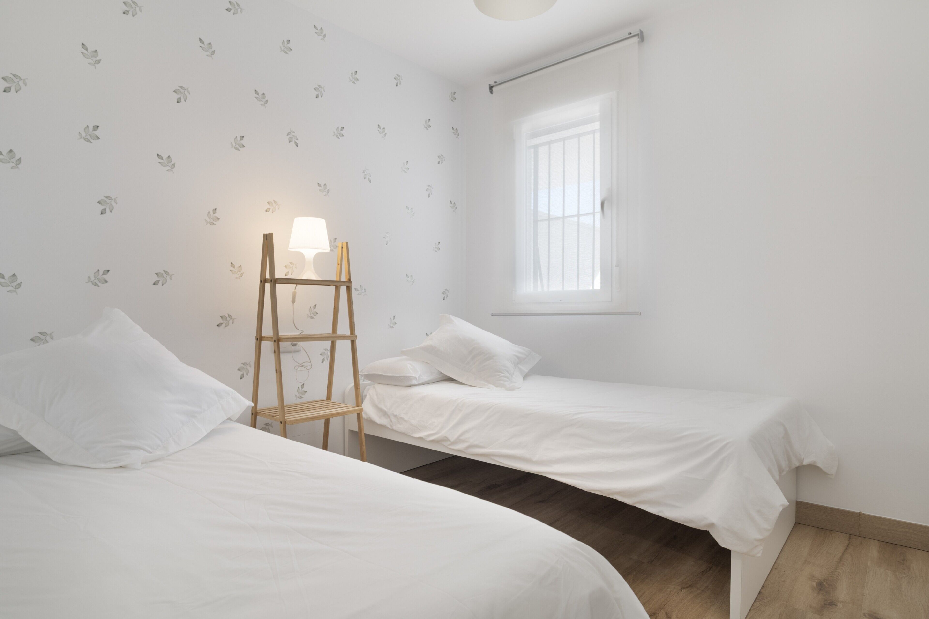 Een slaapkamer met twee eenpersoonsbedden, een houten trap, een raam met luiken en een wand met een bladmotief.