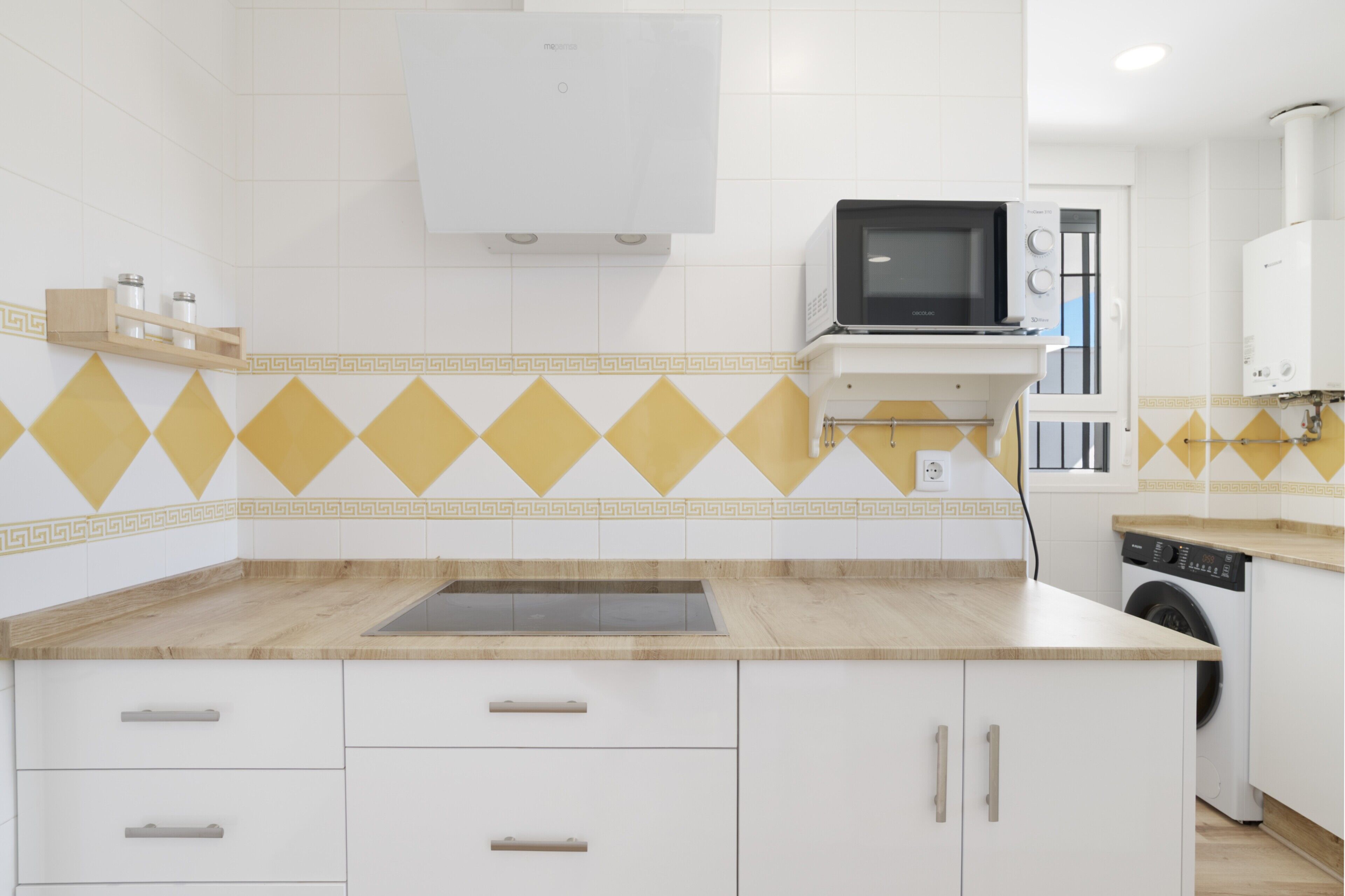 A modern kitchen with white cabinets, a microwave, a washing machine, and a built-in oven.
