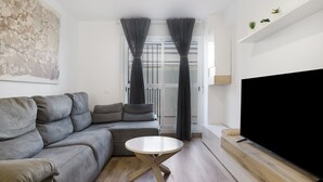 Un salon moderne avec un canapé d’angle gris, une table basse ronde en bois, un téléviseur à écran plat posé sur un meuble en bois, et un grand tableau abstrait accroché au mur.