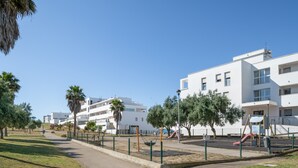 Un quartier résidentiel avec des bâtiments blancs, une aire de jeux dotée de balançoires et de toboggans, et un ciel bleu dégagé.