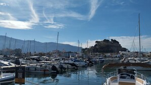 A marina with boats docked, a mountainous backdrop, and a castle-like structure on a hill. - Apartment 'El Palmar' with Sea View, Wi-Fi and Air Conditioning (Denia)
