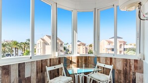 A corner room with a glass table and white chairs, large windows, and a view of other buildings. - Apartment 'El Palmar' with Sea View, Wi-Fi and Air Conditioning (Denia)