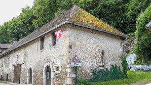 A stone building with a flag, a pedestrian crossing sign, and a distance marker. - Le Portougais, Chanaz – Apartment with Wi-Fi and Air Conditioning (Chanaz)