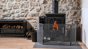 A stone wall, a fireplace with a screen, and a log shelf. - Le Portougais, Chanaz – Apartment with Wi-Fi and Air Conditioning (Chanaz)