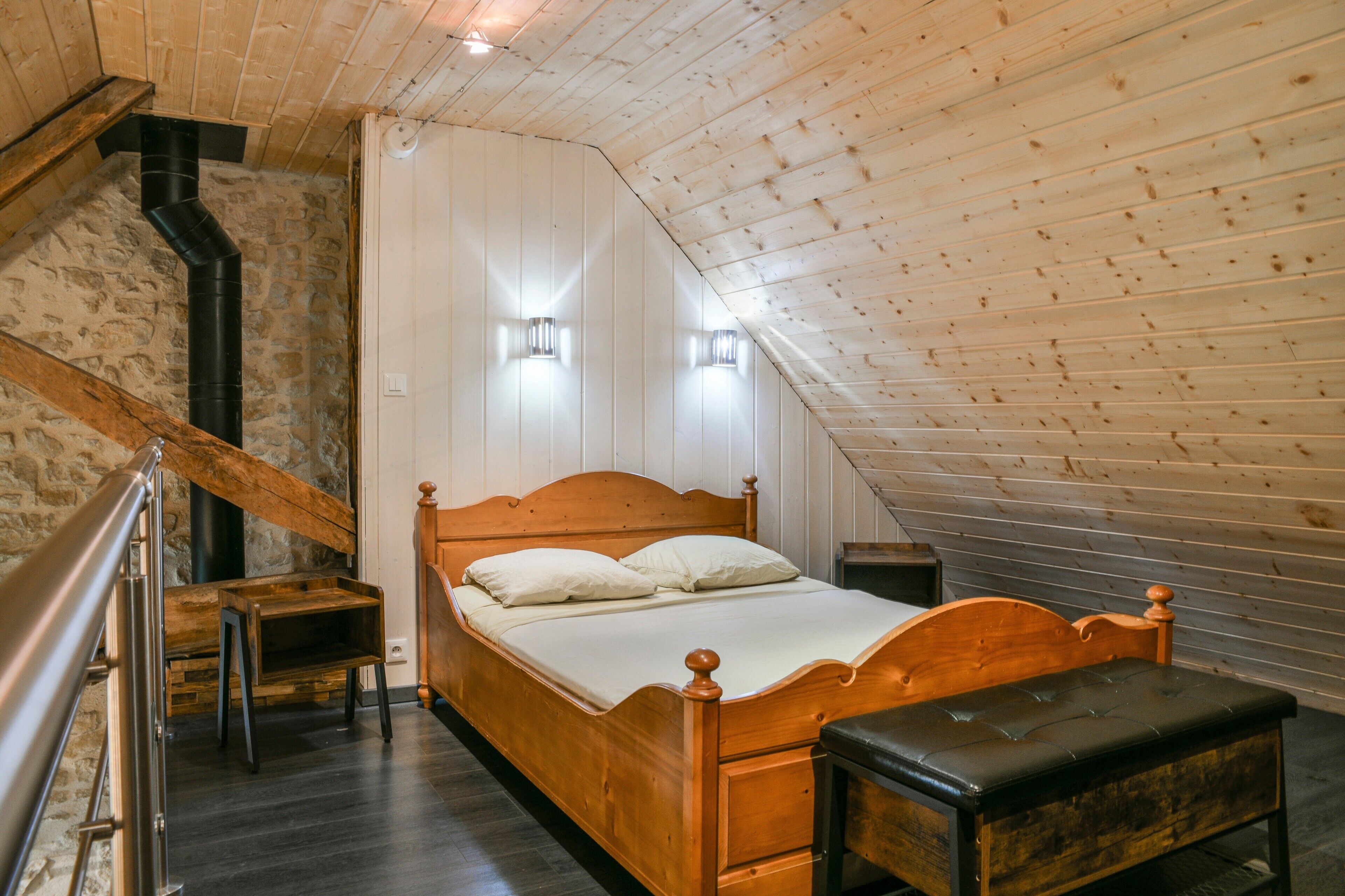 Ein Zimmer mit Holzbalken, einem Bett, einer Bank und einer Steinwand.