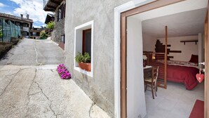 Eine schmale Gasse, die zu einem Gebäude führt, mit einem sichtbaren Schlafzimmer, einem kleinen Fenster mit Pflanze und einer Treppe.