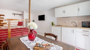 Ein Zimmer mit einem hölzernen Bett, einem Esstisch mit weißer Spitze, einer roten Vase mit Blumen und einer Küchenzeile mit weißen Schränken und einer Mikrowelle.