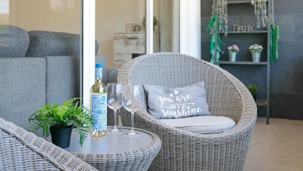 A wicker chair with a cushion, a bottle of water, two glasses, and a small potted plant on a table. - 'Boliche' Apartment with Shared Pool, Wi-Fi, and Air Conditioning (Alicante (Alacant))