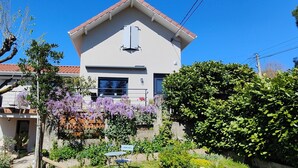 A modern two-story house with a balcony, surrounded by lush greenery and flowering plants. - Green Room with Private Terrace, Wi-Fi, and Air Conditioning (Chozeau)