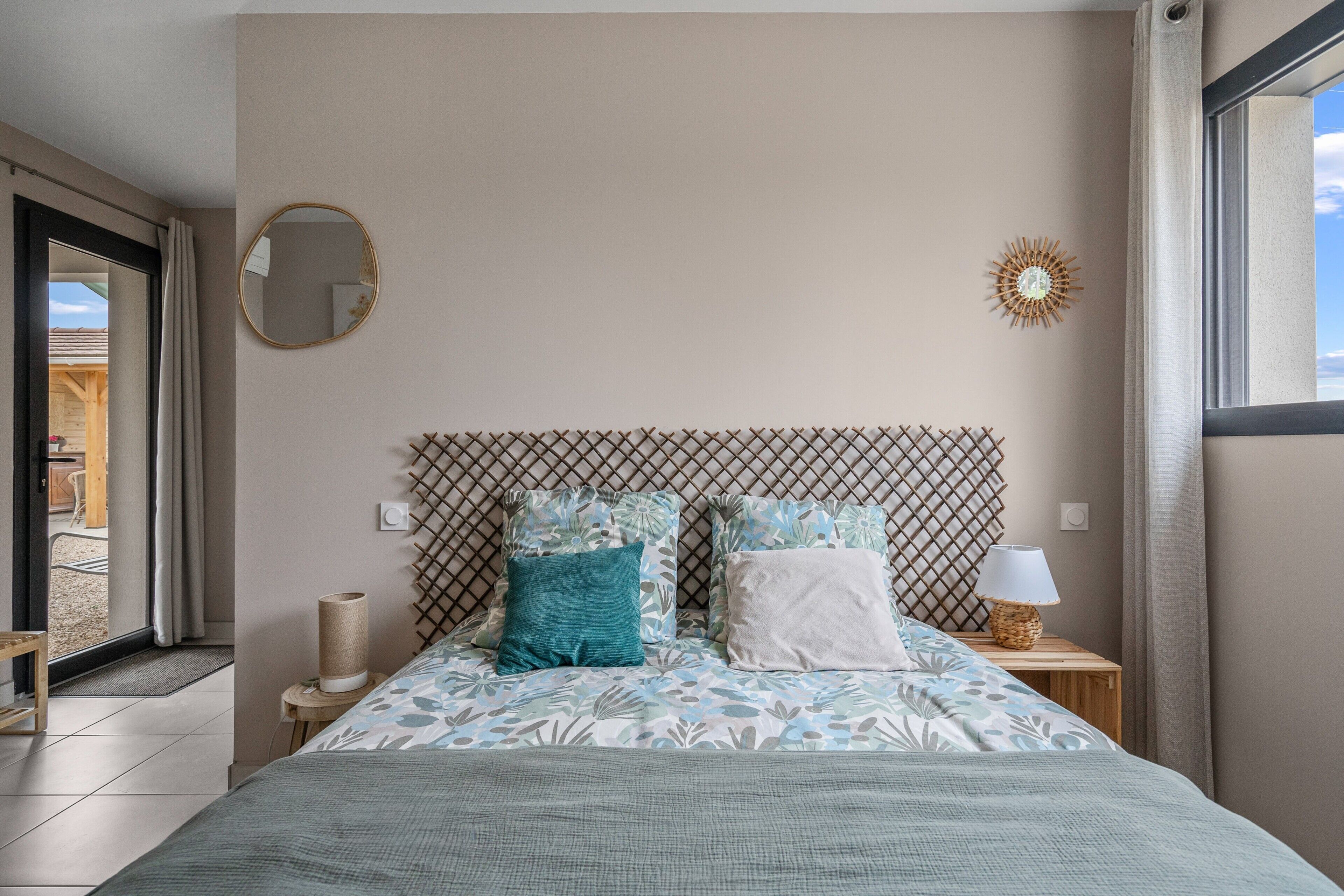 Une chambre à coucher avec un lit, une table de chevet, une lampe, un miroir et une fenêtre.