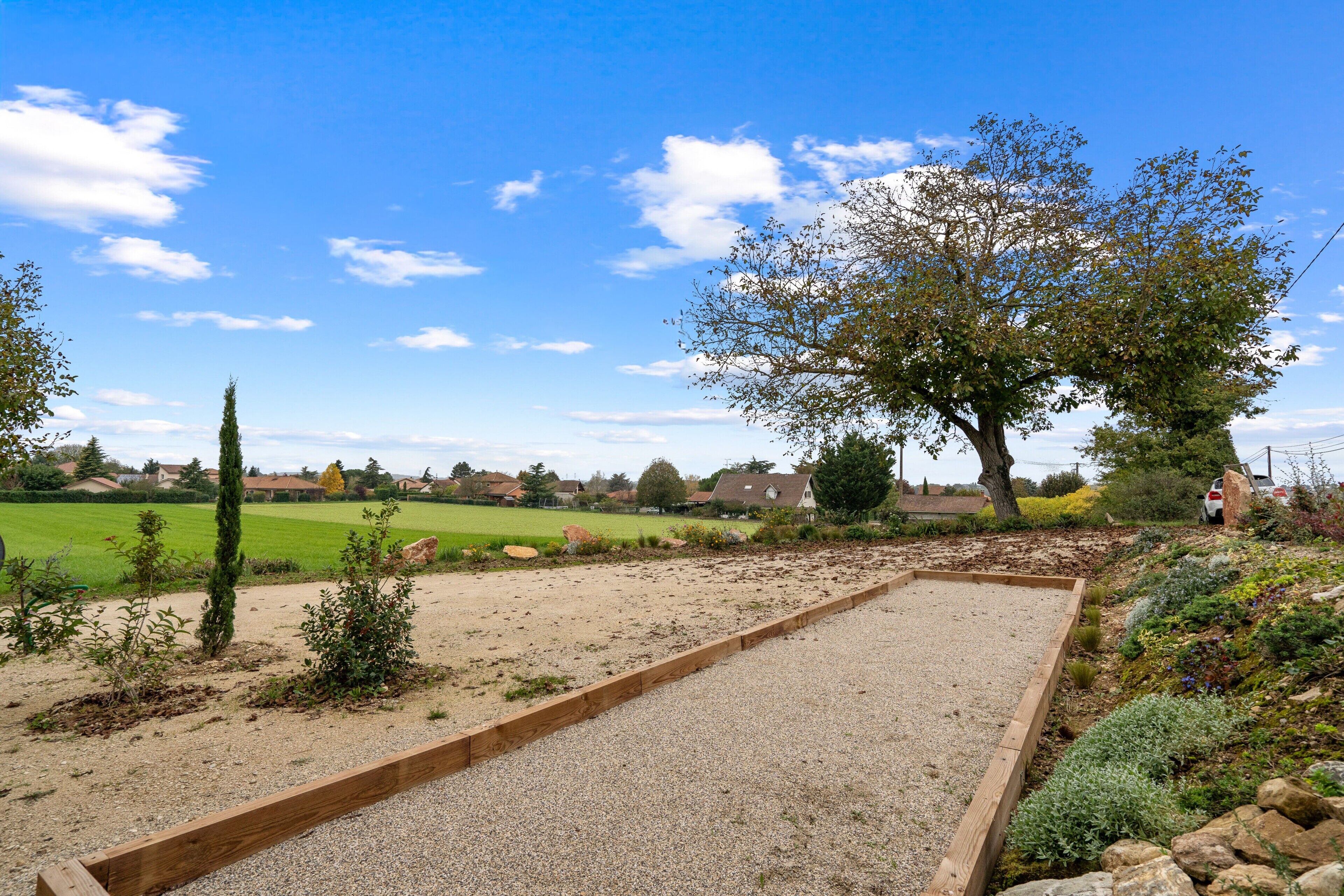 Ein Garten mit einem hölzernen Bereich für Brettspiele, einem großen Baum und einem grünen Feld im Hintergrund.