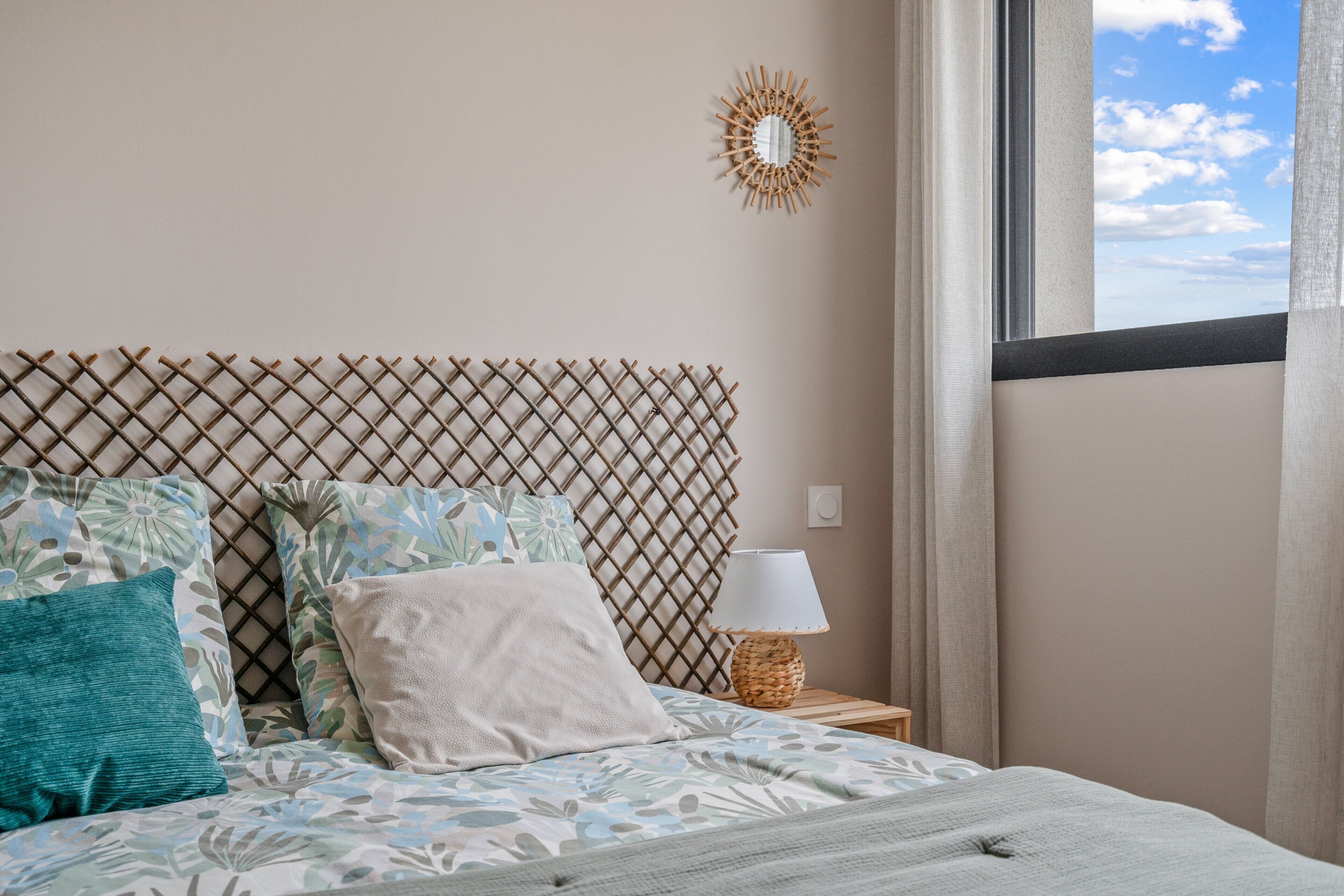 Un lit avec une literie à motifs, une tête de lit en bois, une lampe de chevet et une fenêtre avec des rideaux.