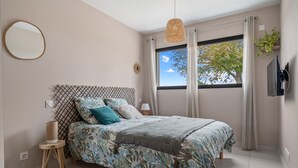 A bedroom with a bed, a bedside lamp, a round mirror, a window with curtains, and a wall-mounted TV. - Green Room with Private Terrace, Wi-Fi, and Air Conditioning (Chozeau)