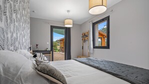 Une chambre à coucher avec un lit, un porte-manteau suspendu, une fenêtre donnant sur un paysage agréable et une porte menant à l’extérieur.