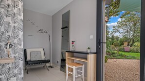 Une pièce comprenant un banc, un petit tabouret, un miroir et une vue sur un jardin, visible à travers une porte vitrée.
