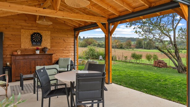 Un intérieur en bois comprenant un coin repas, un jeu de fléchettes et une vue sur un paysage verdoyant.
