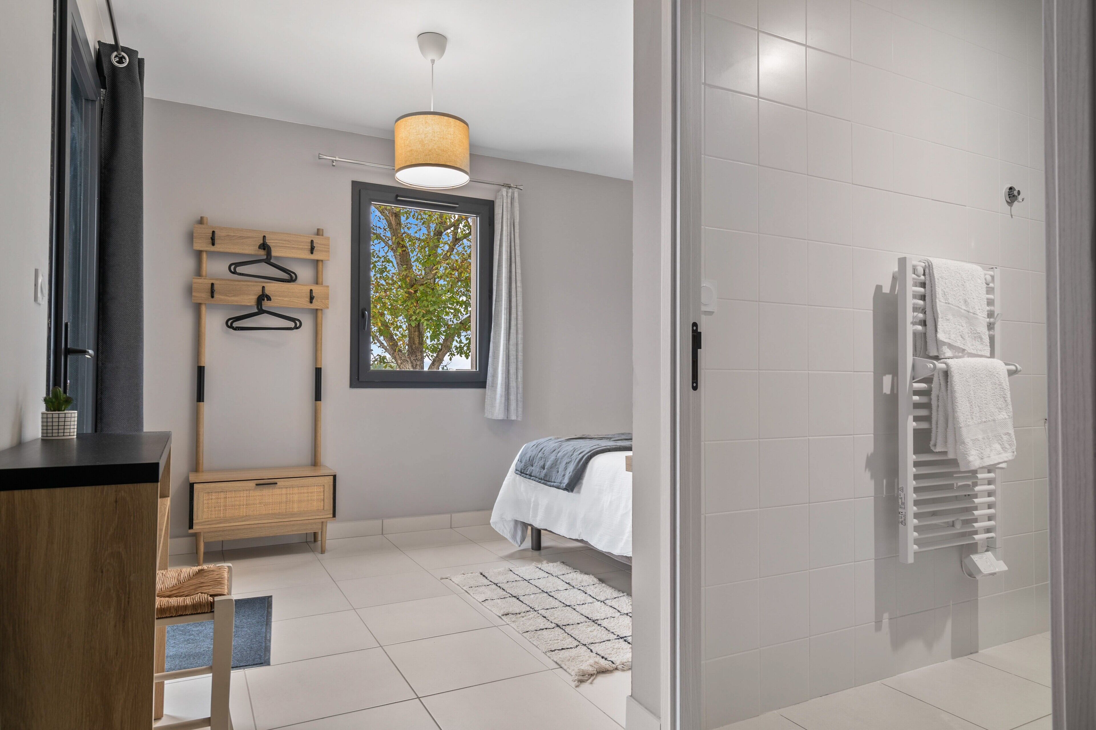 A modern bathroom with a shower, a towel rack, and a window with a view of trees.