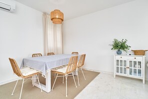 A dining area with a table set for six, surrounded by wicker chairs, a white cabinet with glass doors, and a hanging wicker light fixture. - Apartment 'Balcón Del Mar' with Sea Views, Wi-Fi and Air Conditioning (La Herradura)