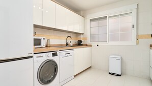 A modern kitchen with white cabinets, a microwave, a coffee maker, a washing machine, and a trash bin. - Apartment 'Balcón Del Mar' with Sea Views, Wi-Fi and Air Conditioning (La Herradura)