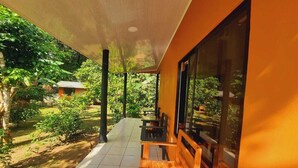 A covered outdoor seating area with wooden benches and a glass wall, surrounded by greenery and a tiled floor. - corcovado green parrot (Drake Bay)