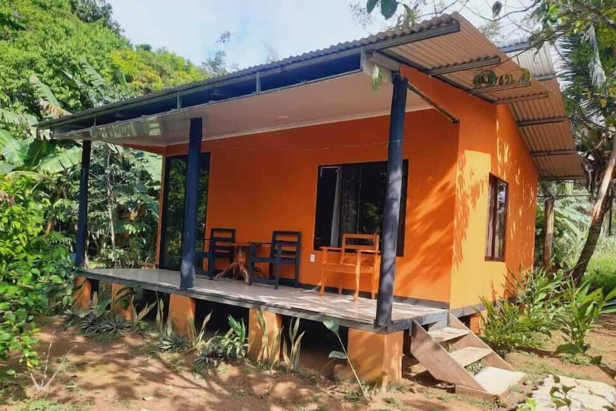 Un pequeño edificio naranja con un porche cubierto y dos sillas de madera.