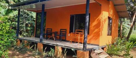 A small, orange building with a covered porch and two wooden chairs.
