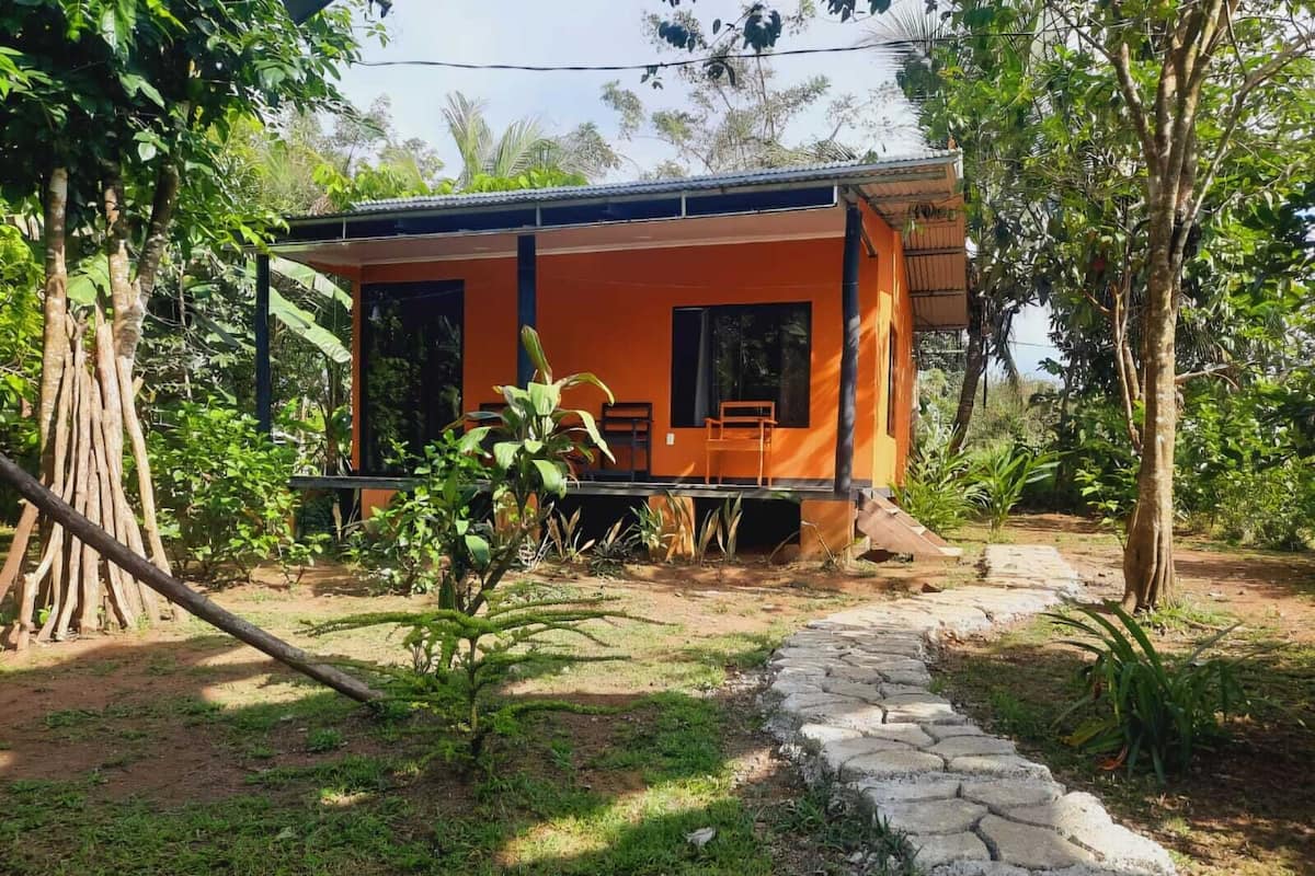 Un edificio de una sola planta con fachada naranja, un porche cubierto y un camino de piedra que conduce a la entrada.
