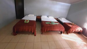 A room with three beds, each with a red bedspread and white pillows. There is a door on the left and a window on the right. - corcovado green parrot (Drake Bay)