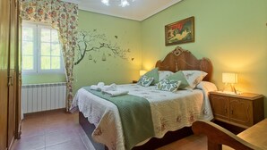 Ein Schlafzimmer mit Bett, Nachttisch, Lampe, Fenster mit Vorhängen, Heizkörper und einer Wand mit Baum-Mural.