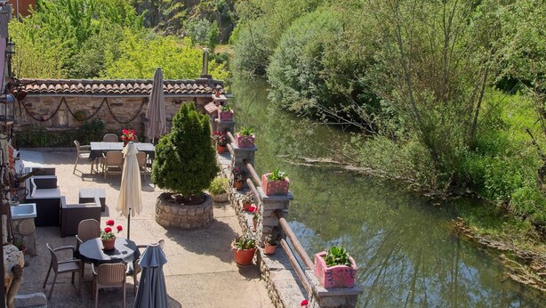 Eine Terrasse im Freien mit Tischen und Stühlen, einer Steinmauer und einem Fluss.