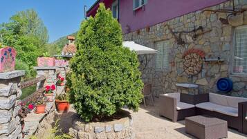 A stone wall with a potted tree, outdoor furniture, and a stone fireplace.