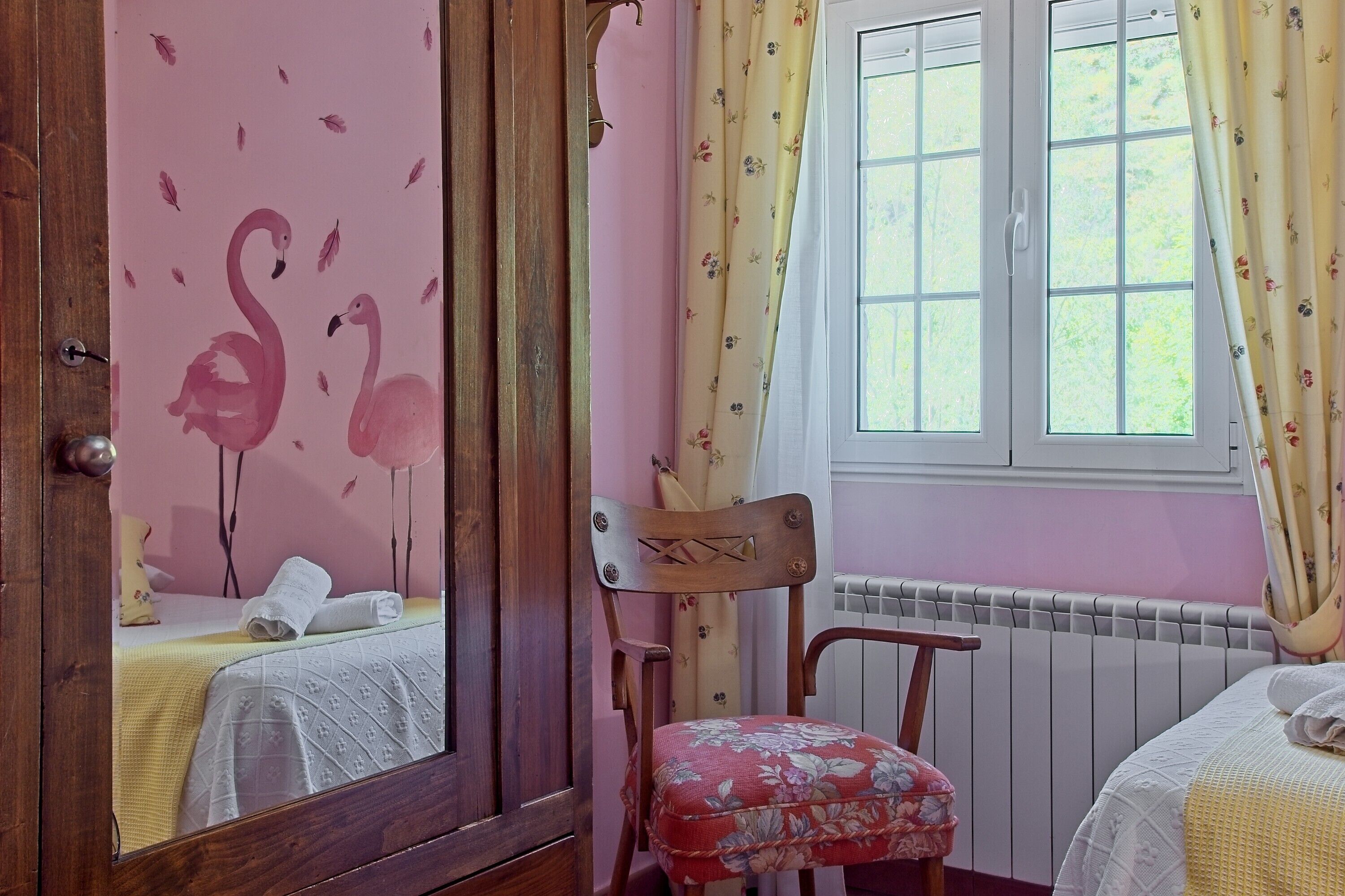 A bedroom with a bed, a chair, a window with curtains, and a radiator.