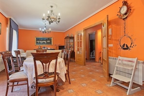 Un comedor con candelabro, sillas de madera, una mesa cubierta con mantel blanco y un reloj en la pared.