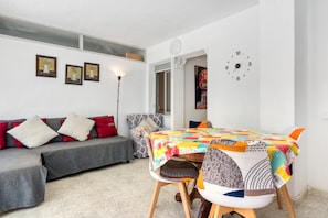 Una sala de estar con un sofá, una mesa con mantel colorido y un reloj de pared.