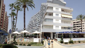 A multi-story hotel with balconies, a restaurant with outdoor seating, and palm trees. - Apartment 'Aguamarina C' with Sea View, Wi-Fi and Air Conditioning (Calpe)