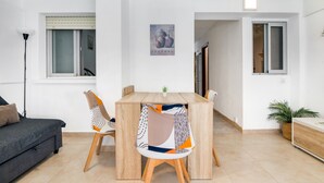 A modern living room with a sofa, a dining table, and chairs. There is a window with blinds, a painting on the wall, and a plant on the floor. - Apartment 'Aguamarina C' with Sea View, Wi-Fi and Air Conditioning (Calpe)