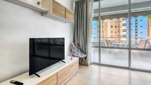 A modern living room with a flat-screen TV, a sofa, a coffee table, and a balcony with a view of buildings. - Apartment 'Aguamarina C' with Sea View, Wi-Fi and Air Conditioning (Calpe)