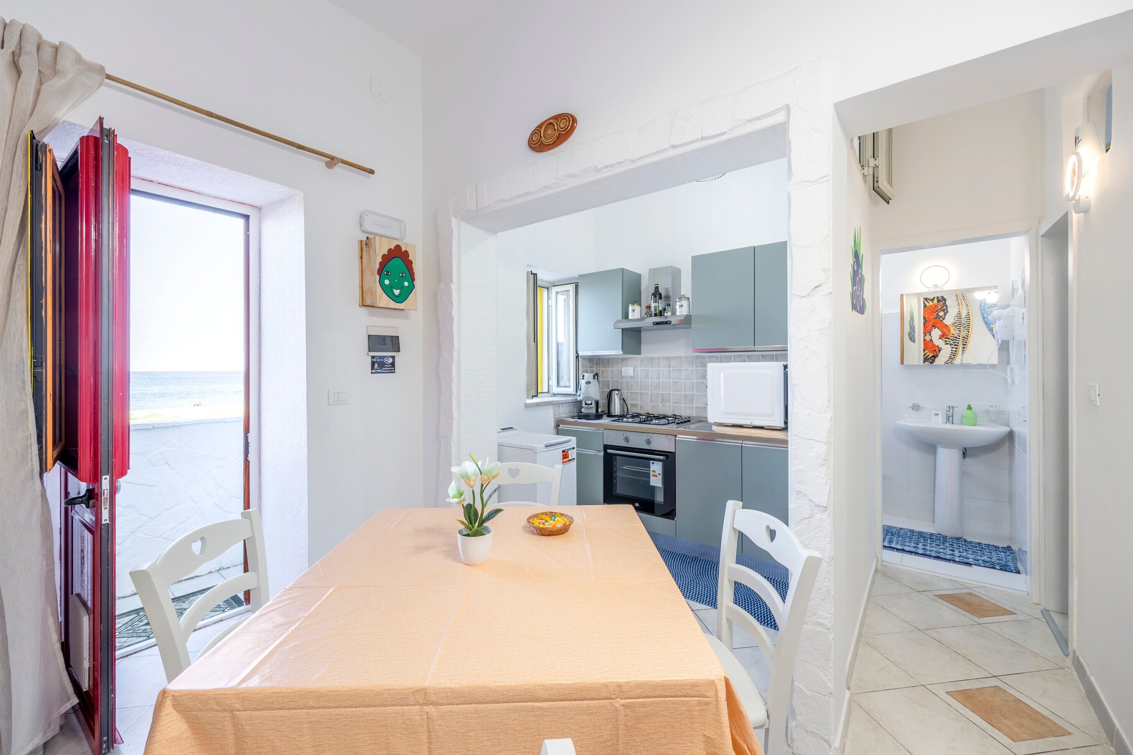A room with a dining table, chairs, a small potted plant, and a view of the sea through an open door.