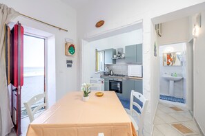 A room with a dining table, chairs, a small potted plant, and a view of the sea through an open door. - Holiday Home 'Coscienza' with Sea View, Wi-Fi and Air Conditioning (Palermo)