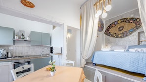 Una habitación de hotel compacta con kitchenette, una cama con colcha azul, un adorno en la pared y un área de comedor con mesa y sillas.