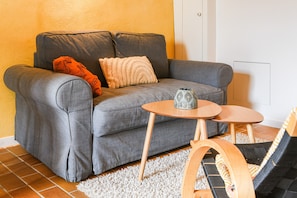 A grey sofa with two pillows, a small wooden table with a decorative item, and a patterned rug.