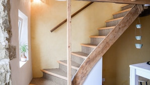 Una escalera de madera con escalones alfombrados, una pared de piedra y una lámpara colgante.