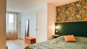 Un dormitorio con cama, espejo, puerta y un papel tapiz decorativo.