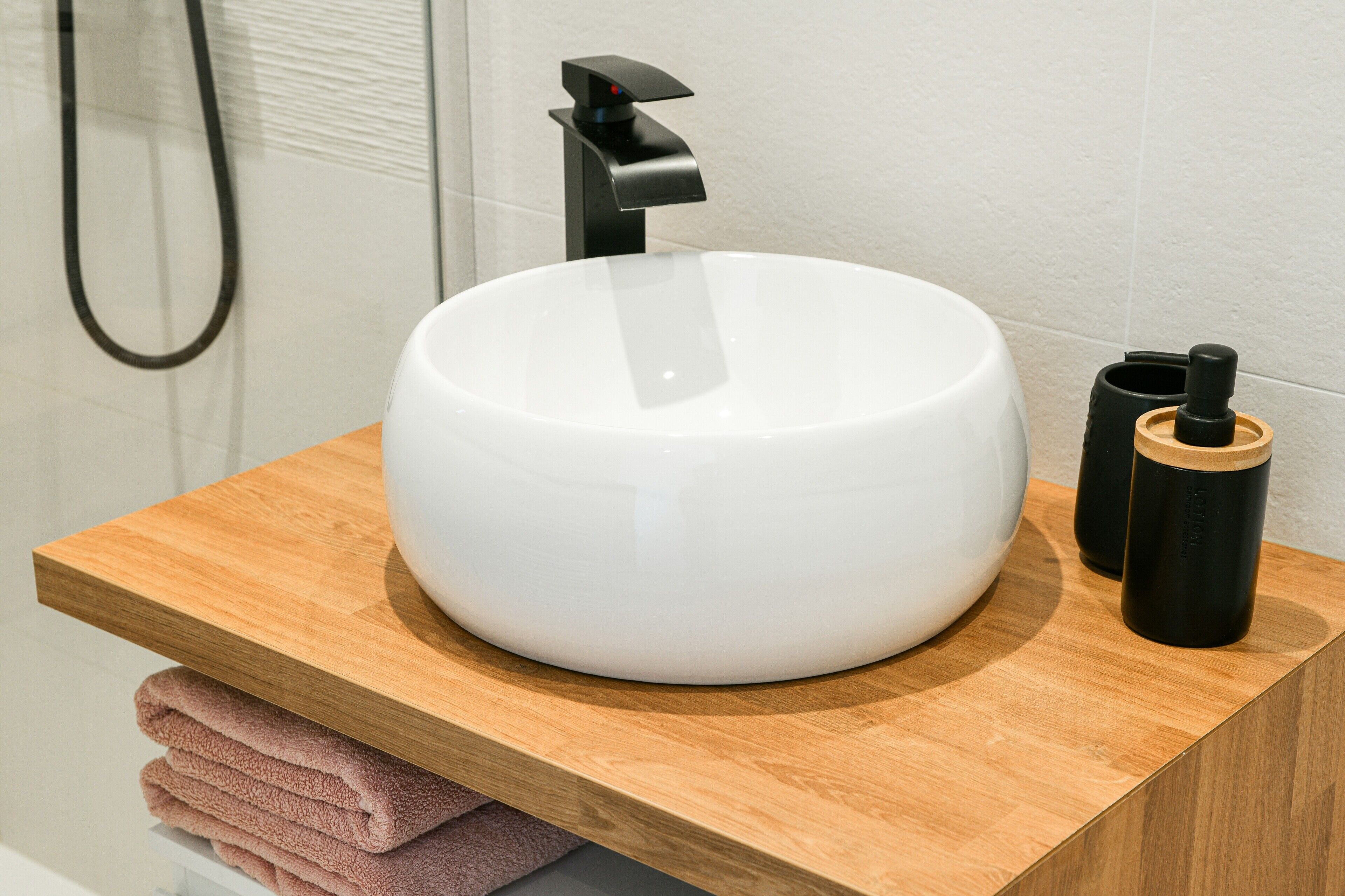 A bathroom with a white sink, a wooden countertop, a black faucet, and a towel rack with folded towels.