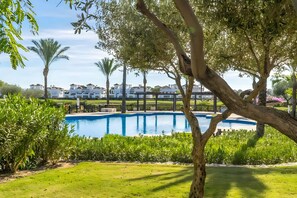 Una piscina rodeada de vegetación y edificios blancos al fondo.